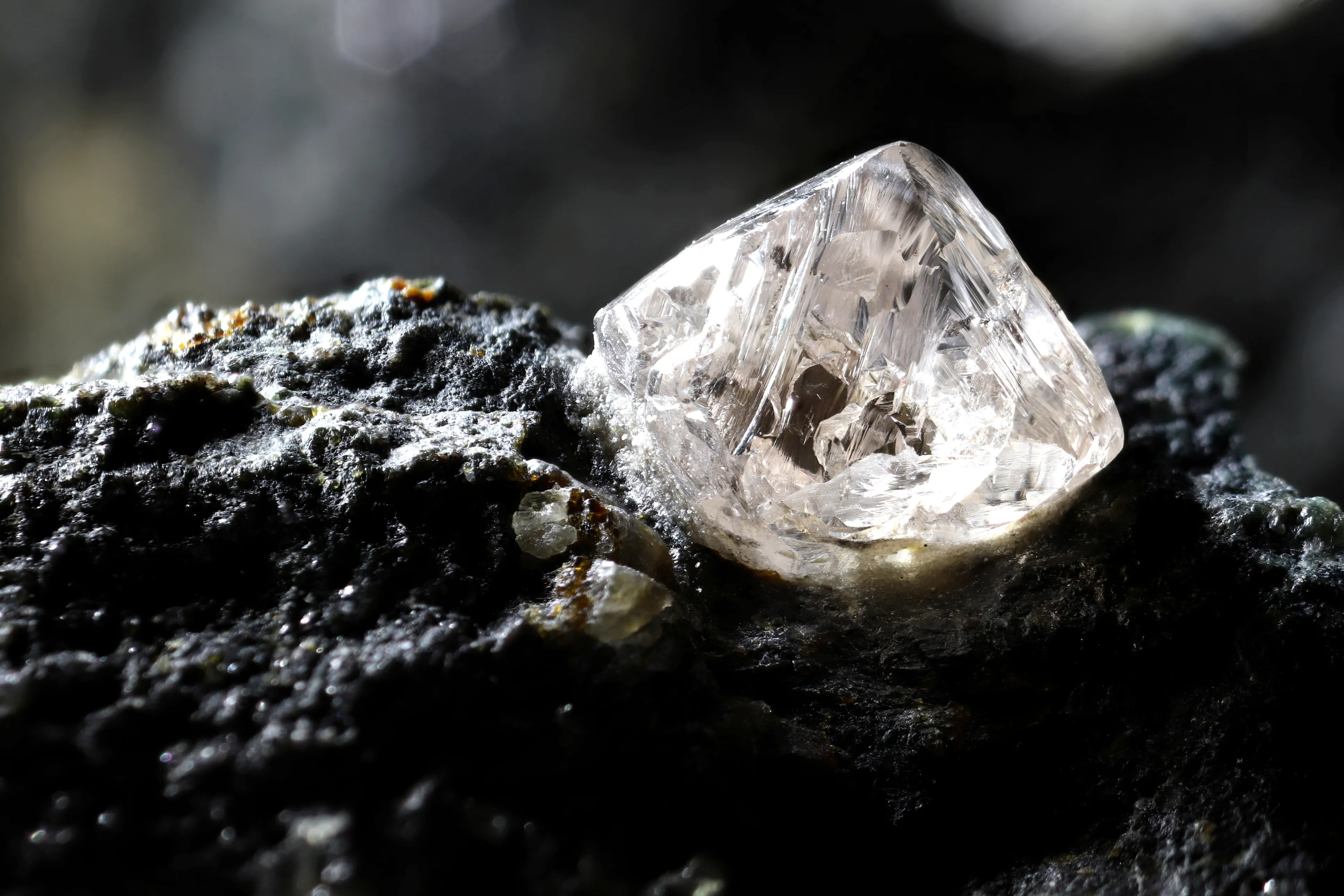 Close-up of a clear, natural, and raw crystal embedded on a dark rock surface.