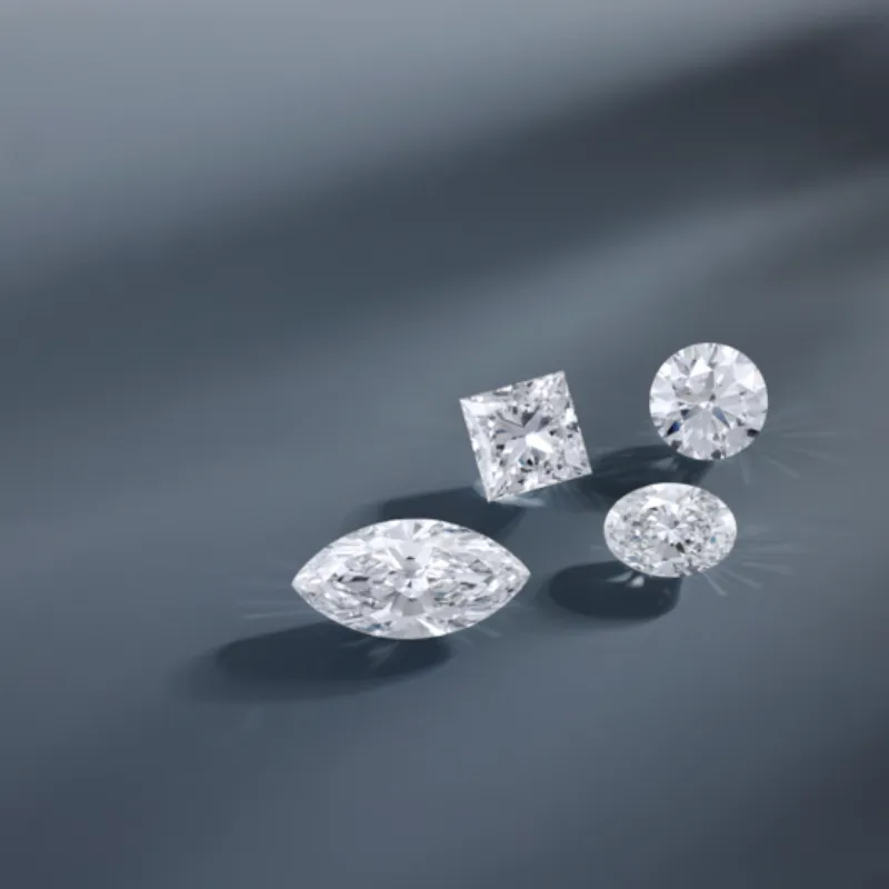 Four sparkling diamonds, princess cut, round, marquise, and oval shapes arranged on a muted blue surface. 