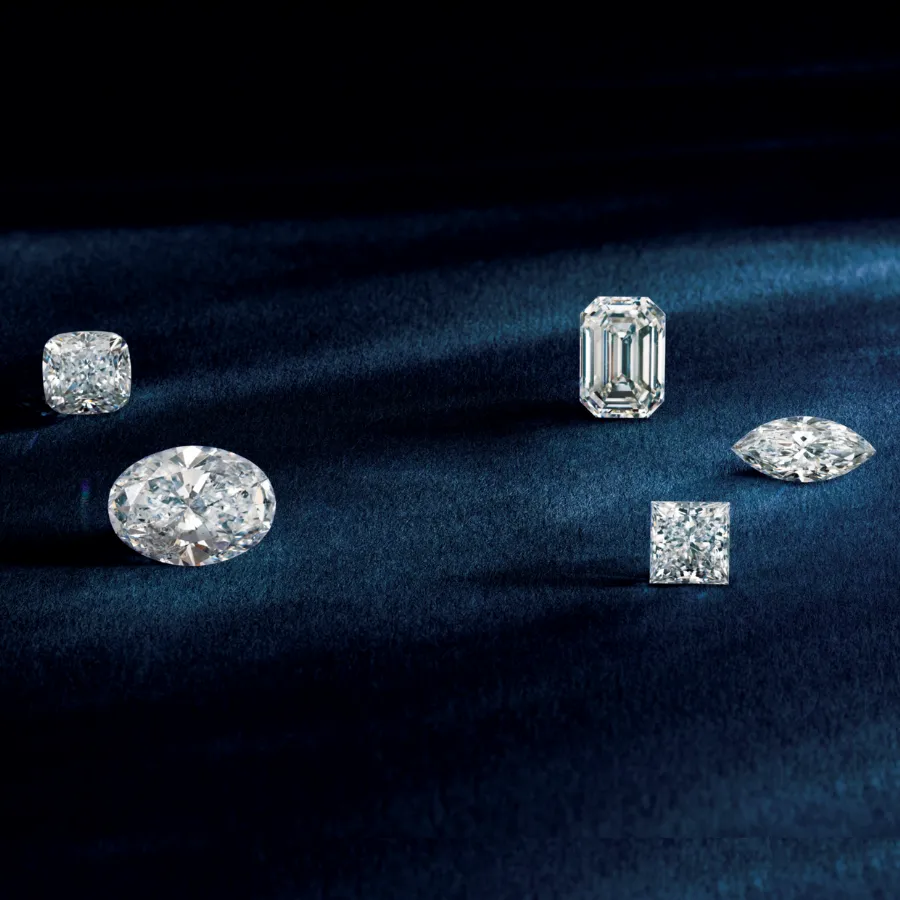 Five sparkling diamonds of various cuts displayed on a dark blue velvet background. Explore Earth-Mined and Lab-Grown Diamonds.