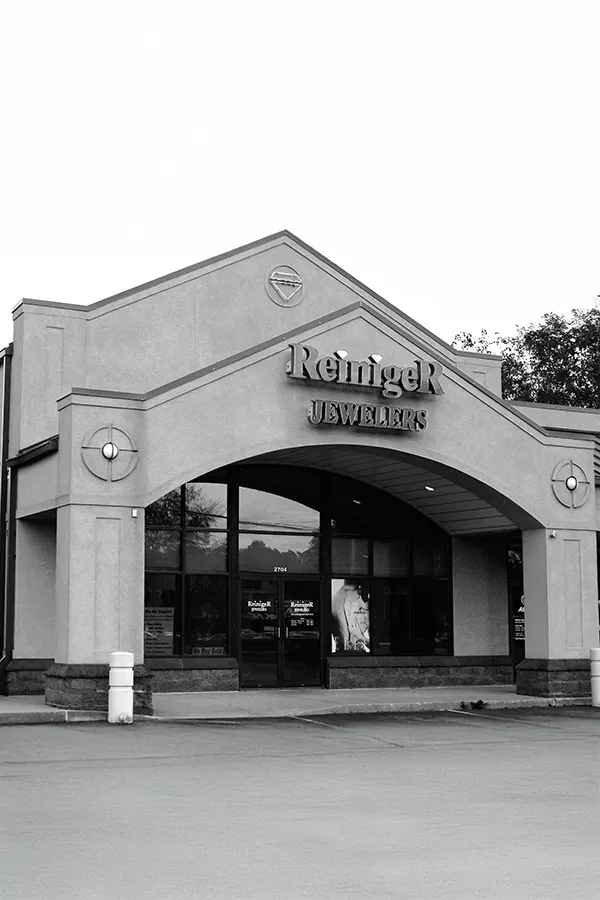 Close-up of a gold engagement ring with a central stone and side diamonds, displayed with a magnifying glass.