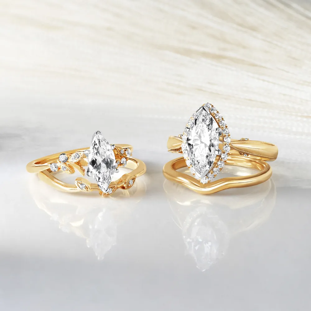 Two elegant gold rings with marquise-cut diamonds, one adorned with smaller diamonds, displayed on a marble surface.