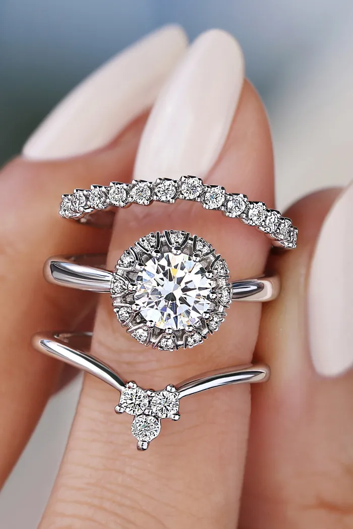 Three elegant diamond rings stacked on a finger, showcasing a central round diamond and two accent bands.