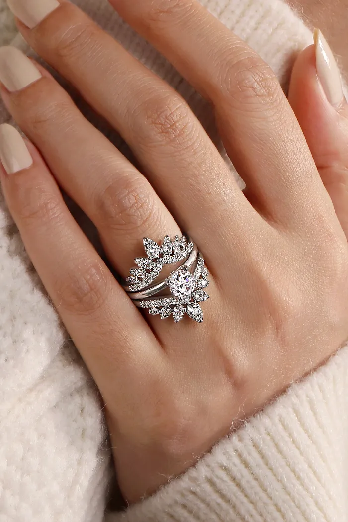 Elegant diamond engagement ring set featuring a central stone and floral accents, displayed on a hand with neutral nail polish.