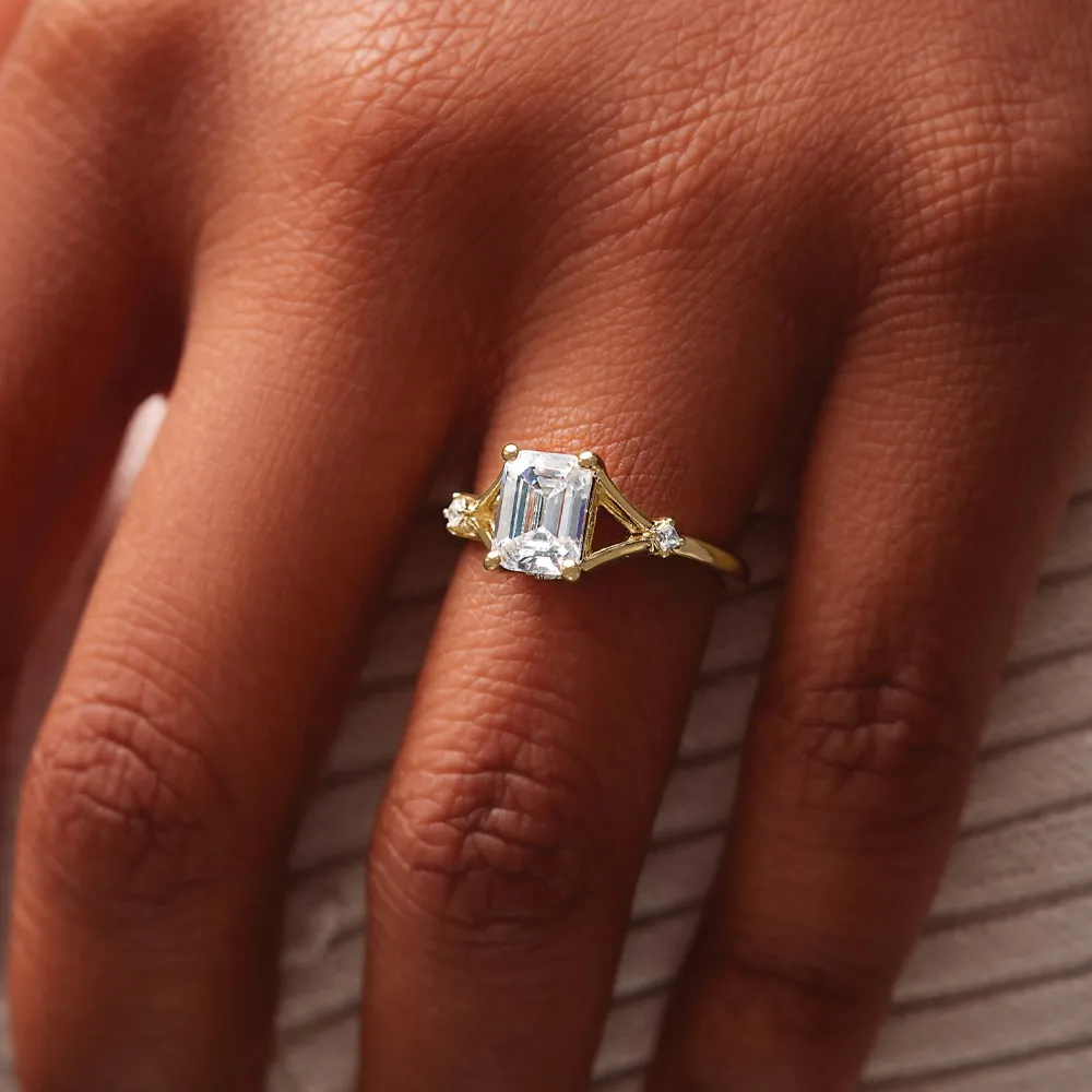 Elegant gold engagement ring with an emerald-cut diamond and side stones, showcased on a hand.