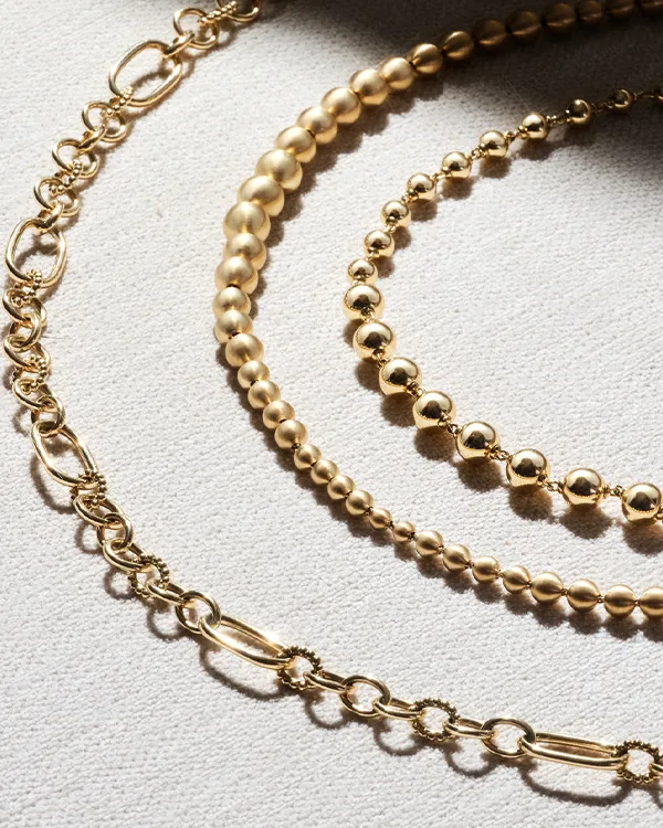 Three elegant gold necklaces of varying styles and sizes displayed on a light fabric background. Shop Now at Reiniger Jewelers.