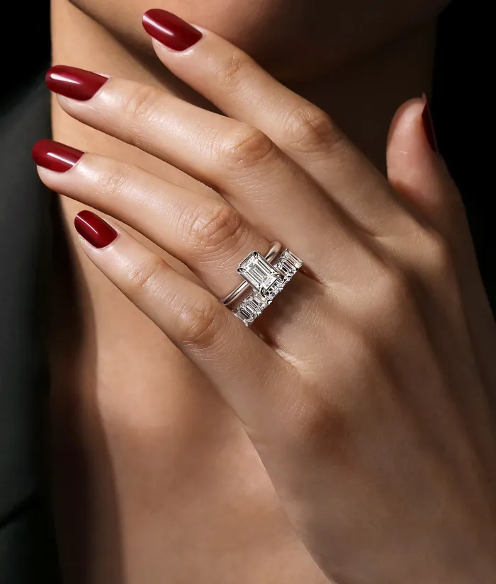 Elegant hand wearing a diamond engagement ring with a rectangular center stone and side stones, showcasing fine jewelry.