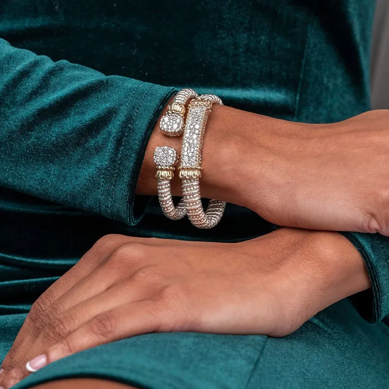 A person wearing two sparkling gold and silver bracelets on their wrist, dressed in a teal velvet outfit.