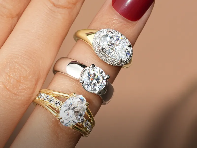 Three gold and silver rings with large oval and round diamonds on a person's fingers.