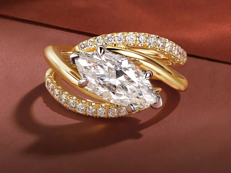 Marquise-cut diamond ring with gold band on a brown surface.