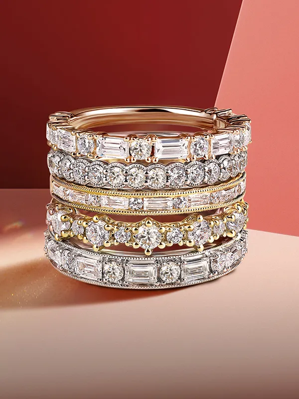 Stacked silver wedding bands with various diamond settings on a light background.