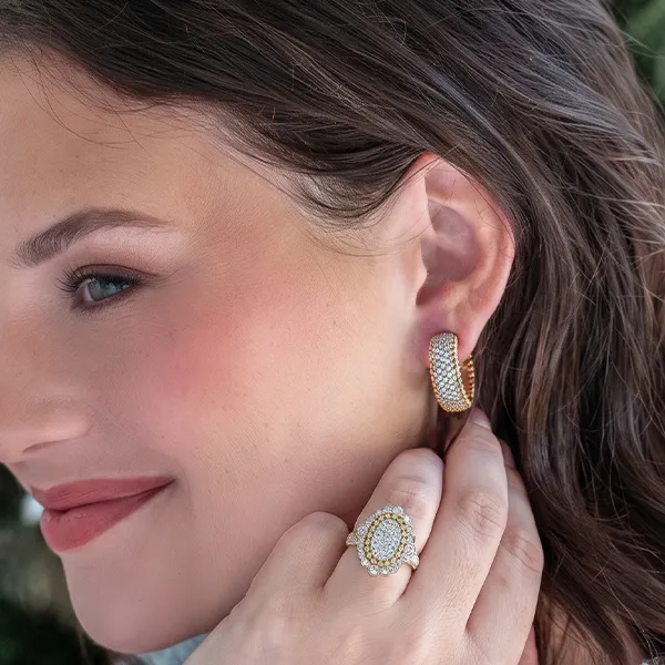 A woman wearing gold hoop earrings and a diamond ring, smiling.