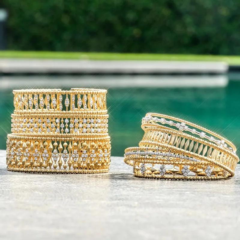 Gold and diamond bangles displayed outdoors near a pool.