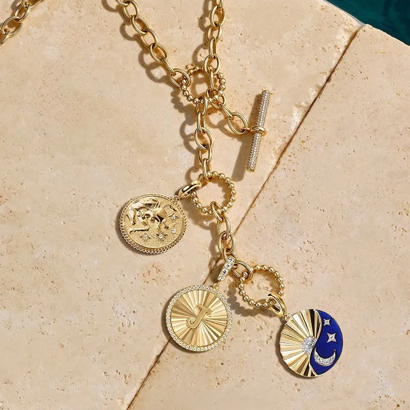 Gold chain necklace with three pendants: a textured coin, a sunburst design, and a crescent moon with stars.