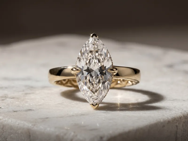 Marquise-cut diamond ring with gold band on marble surface.