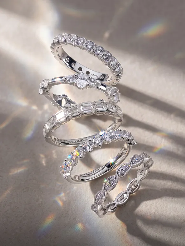 Stacked silver wedding bands with various diamond settings on a light background.