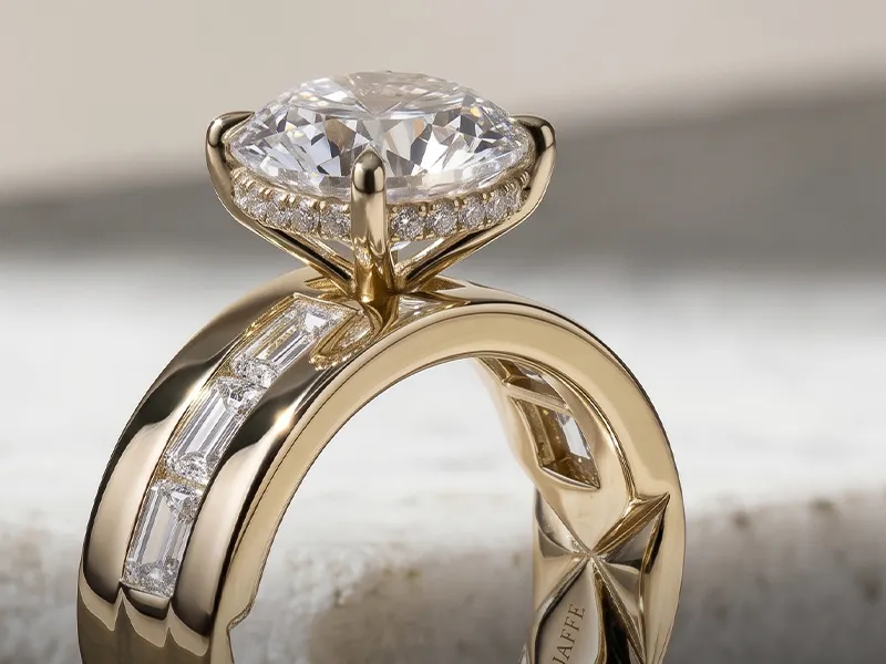 A gold ring with a large diamond and baguette accents on a marble surface.
