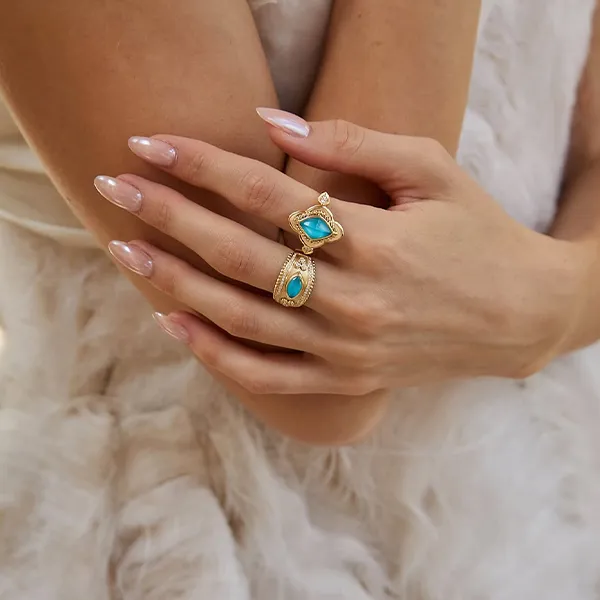 Hands with manicured nails wearing gold rings with turquoise stones.