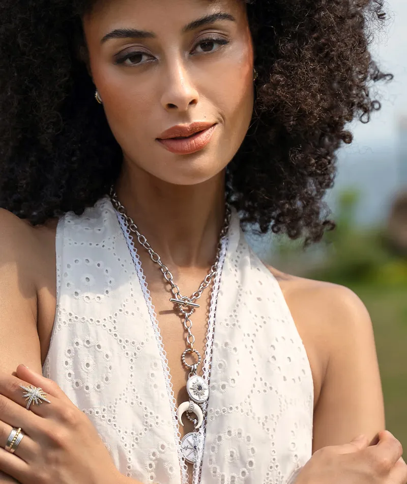 Model wearing a white dress with curly hair, showcasing layered necklaces and rings.