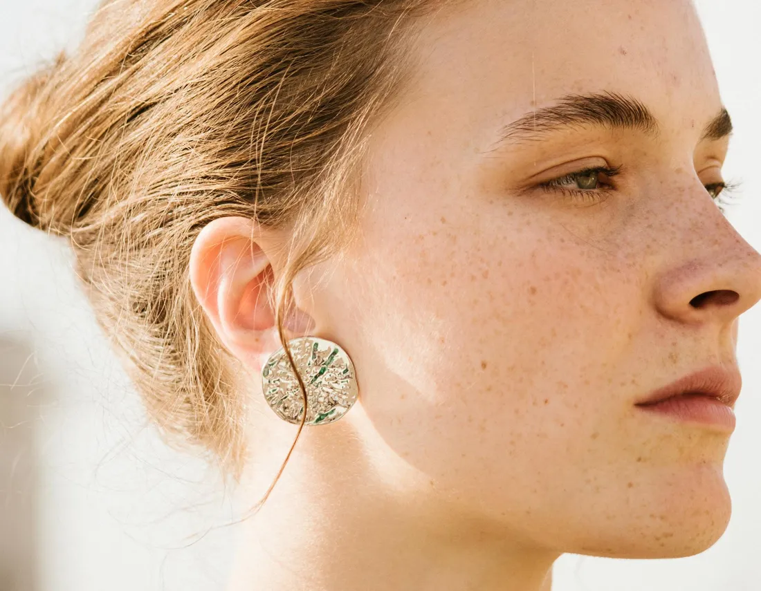 Woman looking to the right wearing silver earring with specks of green in it