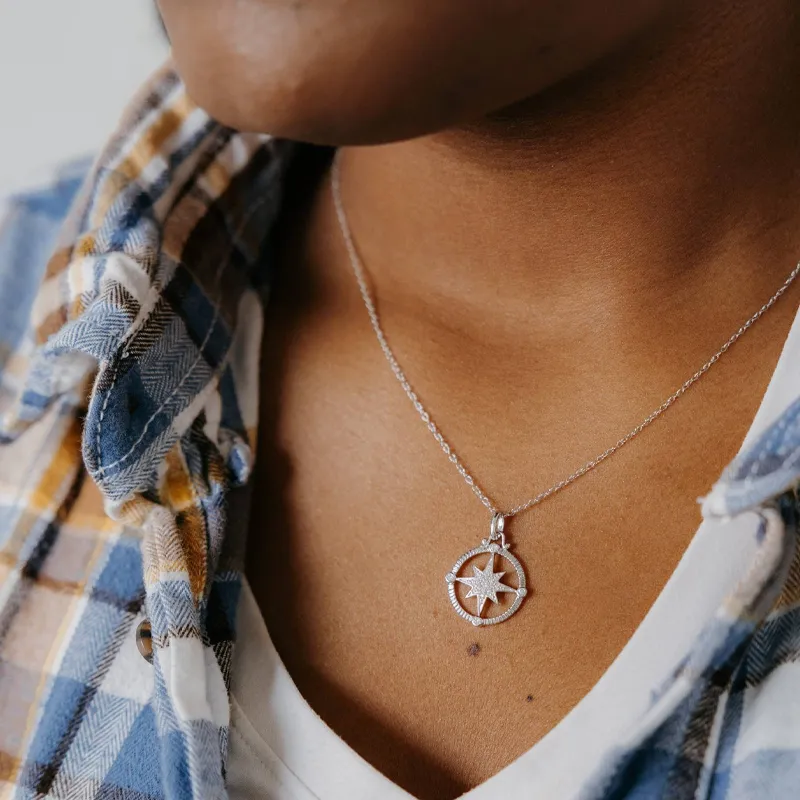 Close-up of a silver compass necklace worn by a model, showcasing elegant jewelry style.