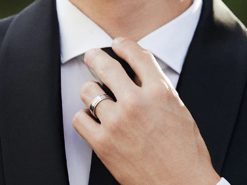 Man adjusting his tie while wearing a wedding band, dressed in a formal suit.