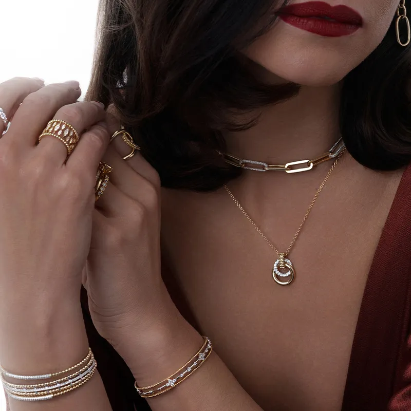 Elegant jewelry display featuring layered necklaces, rings, and bracelets on a model with red lips. Shop at R. Gregory Jewelers.