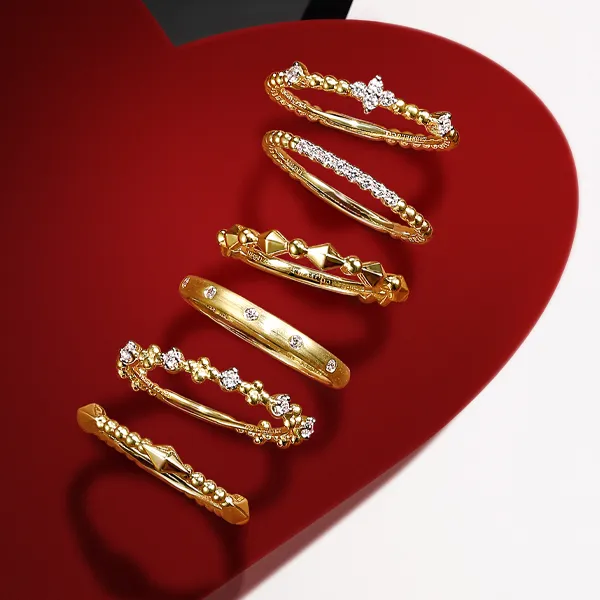 Gold rings with various designs displayed on a red heart background. Click to explore fashion rings at R. Gregory Jewelers.