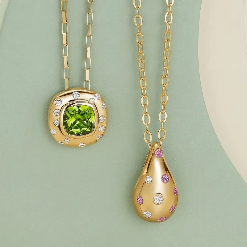 Two gold necklaces with gemstone pendants on a green background.