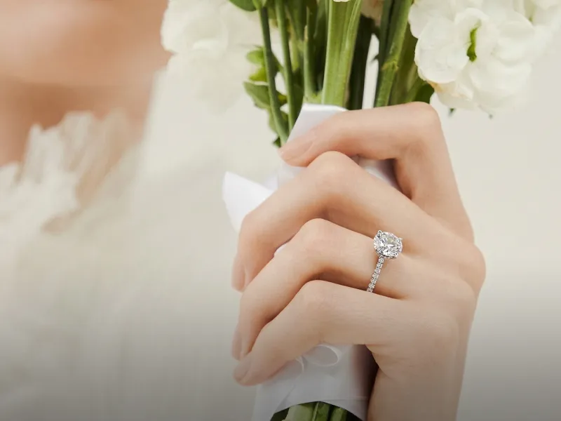 Hand holding a bouquet, showcasing a diamond engagement ring.