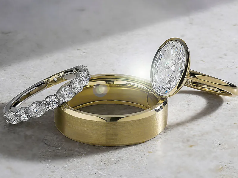 Three elegant rings: a diamond-studded band, a polished gold band, and a large oval diamond ring.