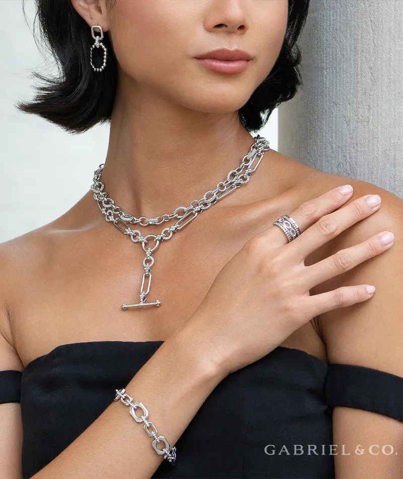 Model wearing layered silver jewelry including a necklace, earrings, bracelet, and rings from R. Gregory Jewelers.