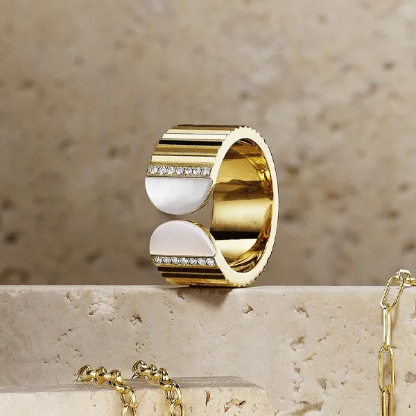 Gold and white ring with diamond accents displayed on a stone surface. Shop fashion rings at R. Gregory Jewelers.