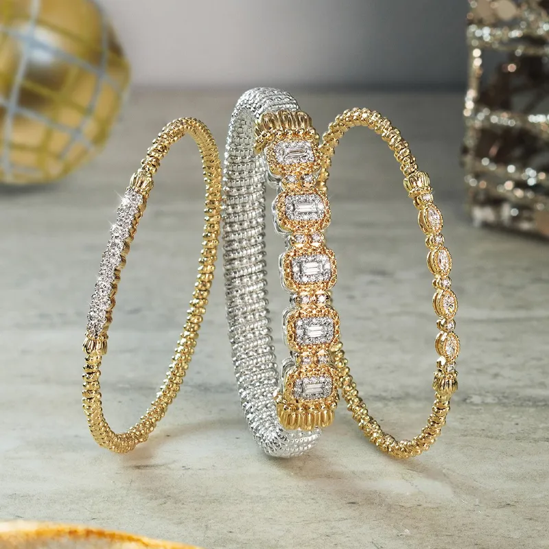 Three elegant bracelets in gold and silver with sparkling details, displayed on a marble surface.