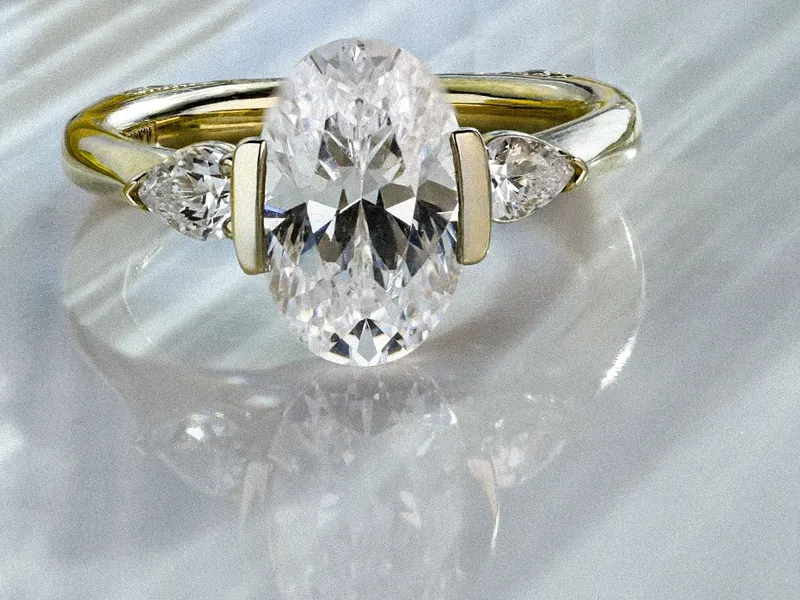 Elegant oval diamond engagement ring with side stones, displayed on a reflective surface. 
