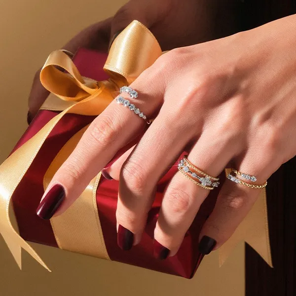 Elegant hand adorned with multiple rings, holding a gift box with a gold ribbon.