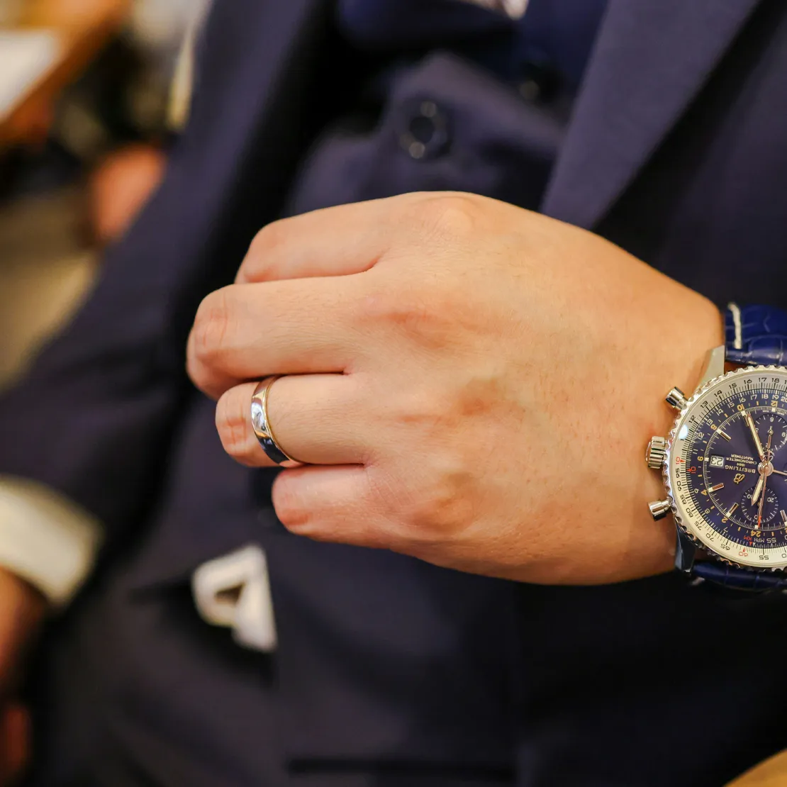 Man in blue suit with watch and wedding ring, gesturing with hand.