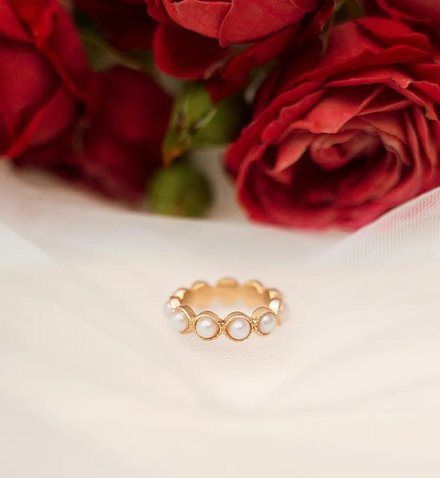 Gold ring with pearls on a soft fabric background, surrounded by red roses. Perfect for a romantic gift.