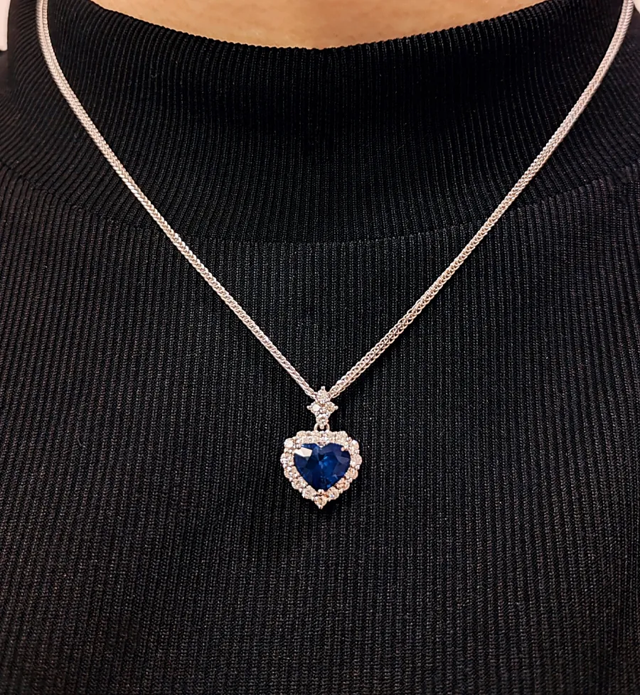 Heart-shaped blue gemstone pendant necklace with diamond accents, worn on a black turtleneck.
