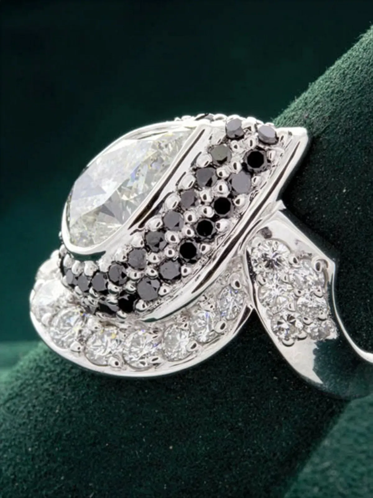 Elegant silver ring featuring a large diamond and black stones, displayed on a green velvet background. Visit Rich Custom Jewelr