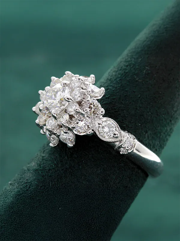 Gold diamond ring with intricate design featuring multiple sparkling stones, displayed on a green velvet stand.