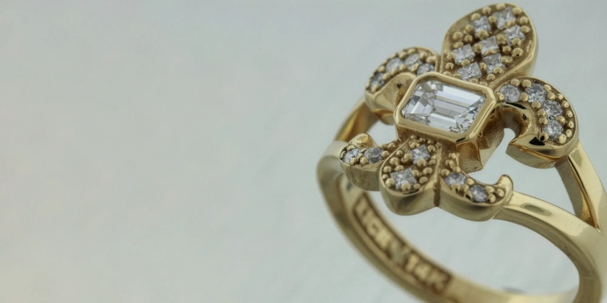 Gold floral ring with a central emerald-cut diamond and smaller diamonds, showcasing intricate design and elegance.