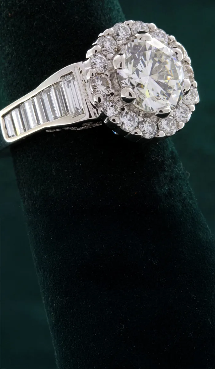 Elegant diamond halo engagement ring with a round center stone and baguette accents, available at Rich Custom Jewelry.