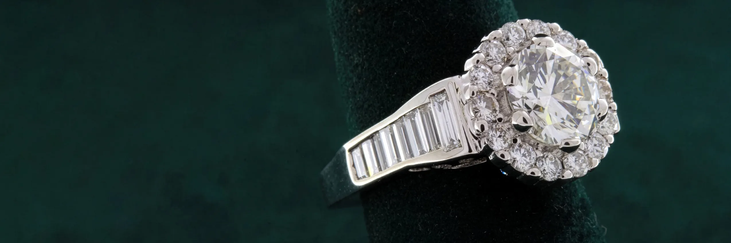 Elegant diamond halo engagement ring with a round center stone and baguette accents, available at Rich Custom Jewelry.