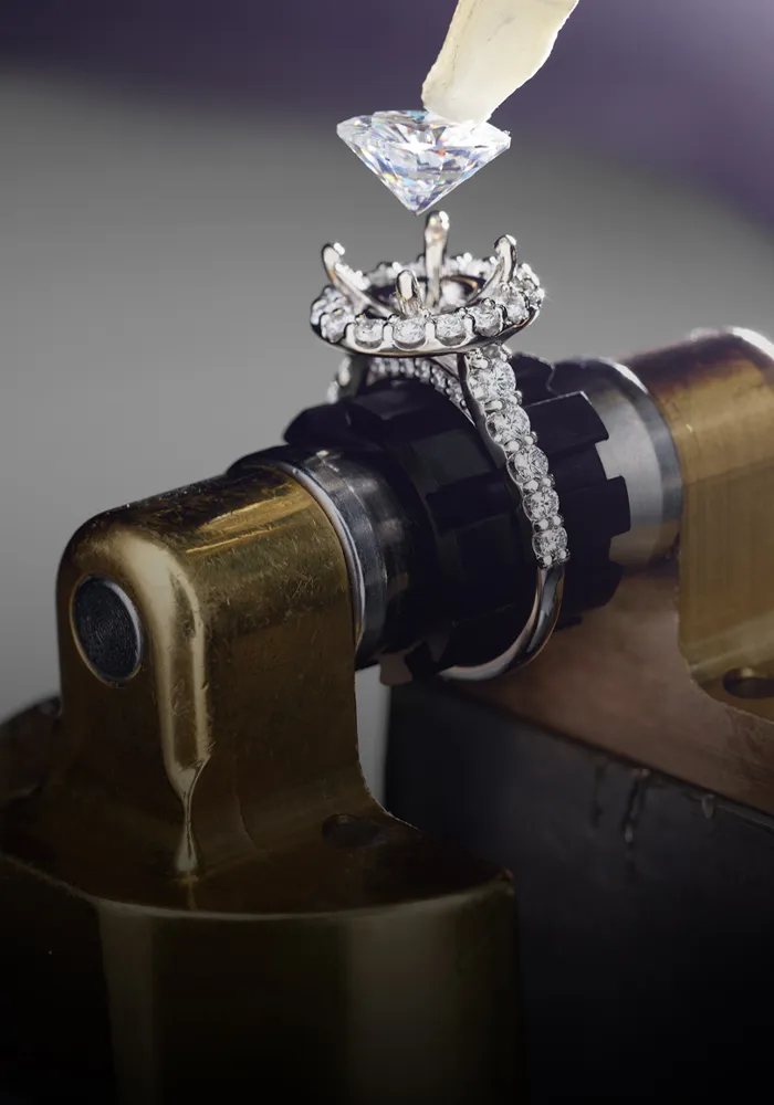 A diamond ring is being set with a diamond using a tool in a jewelry workshop.