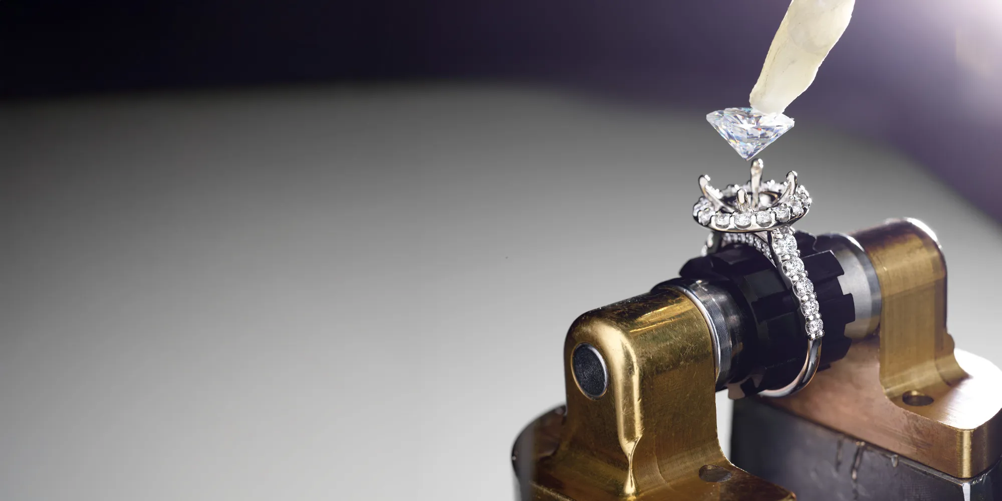 A diamond ring is being set with a diamond using a tool in a jewelry workshop.