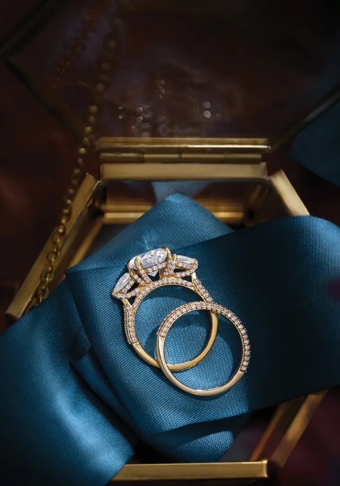 Elegant gold engagement and wedding rings on a teal ribbon, inviting you to shop bridal sets.