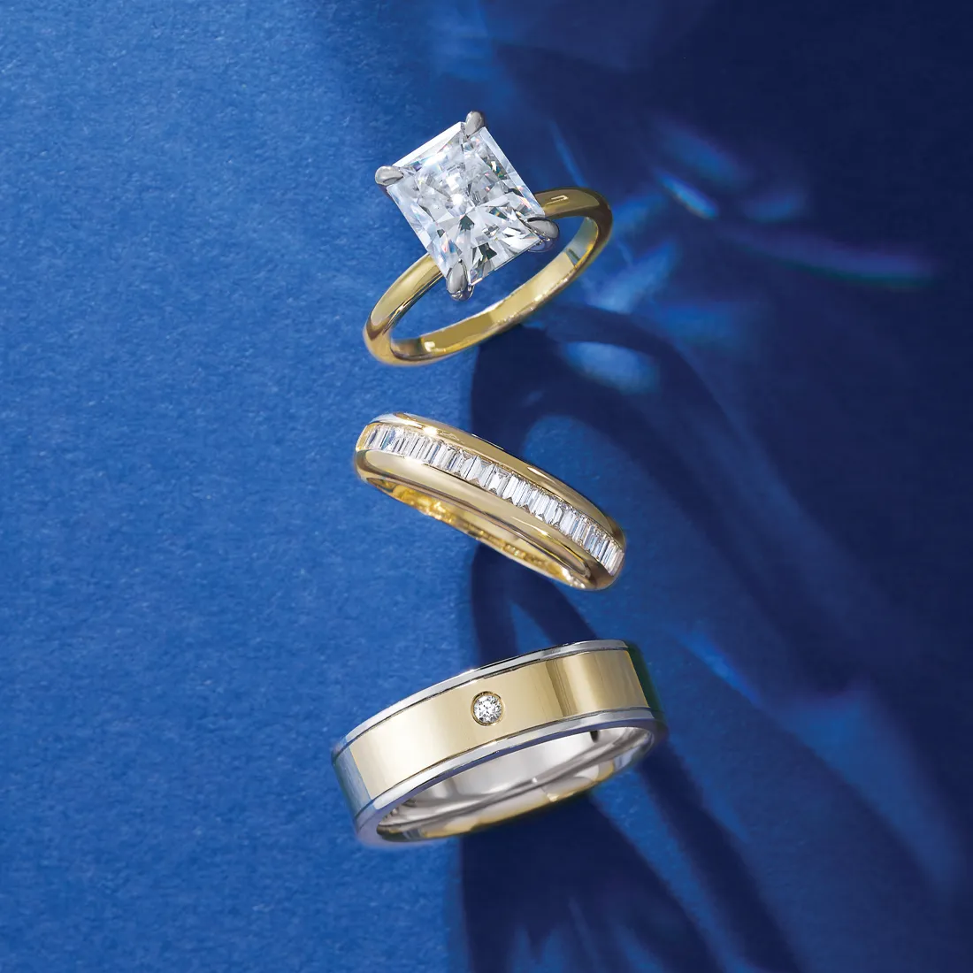 Three elegant rings featuring a central emerald-cut diamond, set against a blue background.