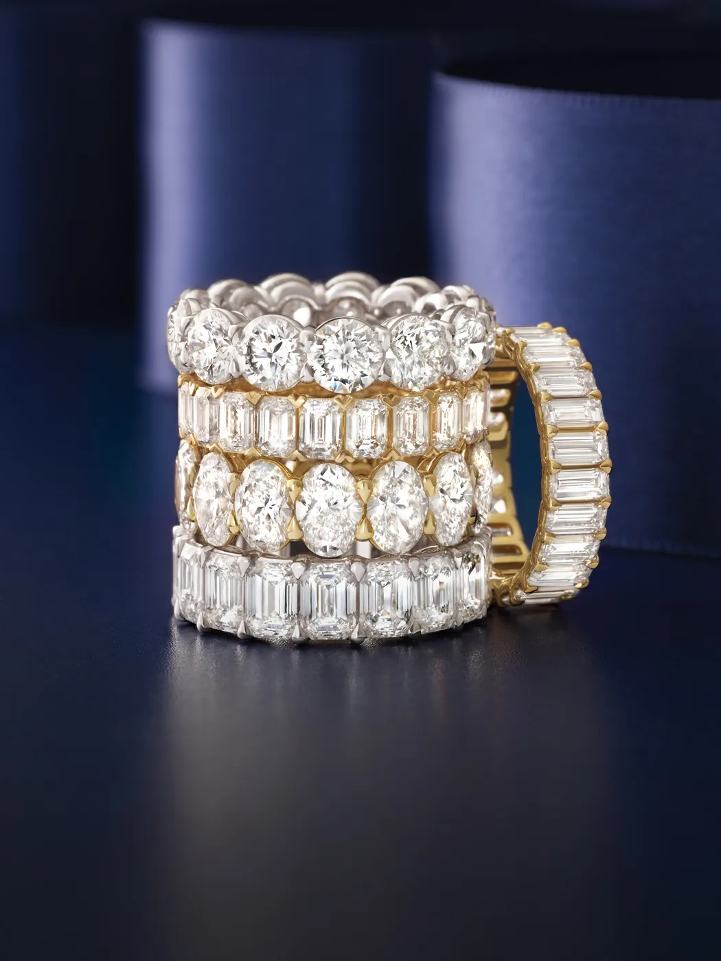 Three elegant diamond rings stacked together, showcasing round and emerald-cut stones in gold and silver settings.