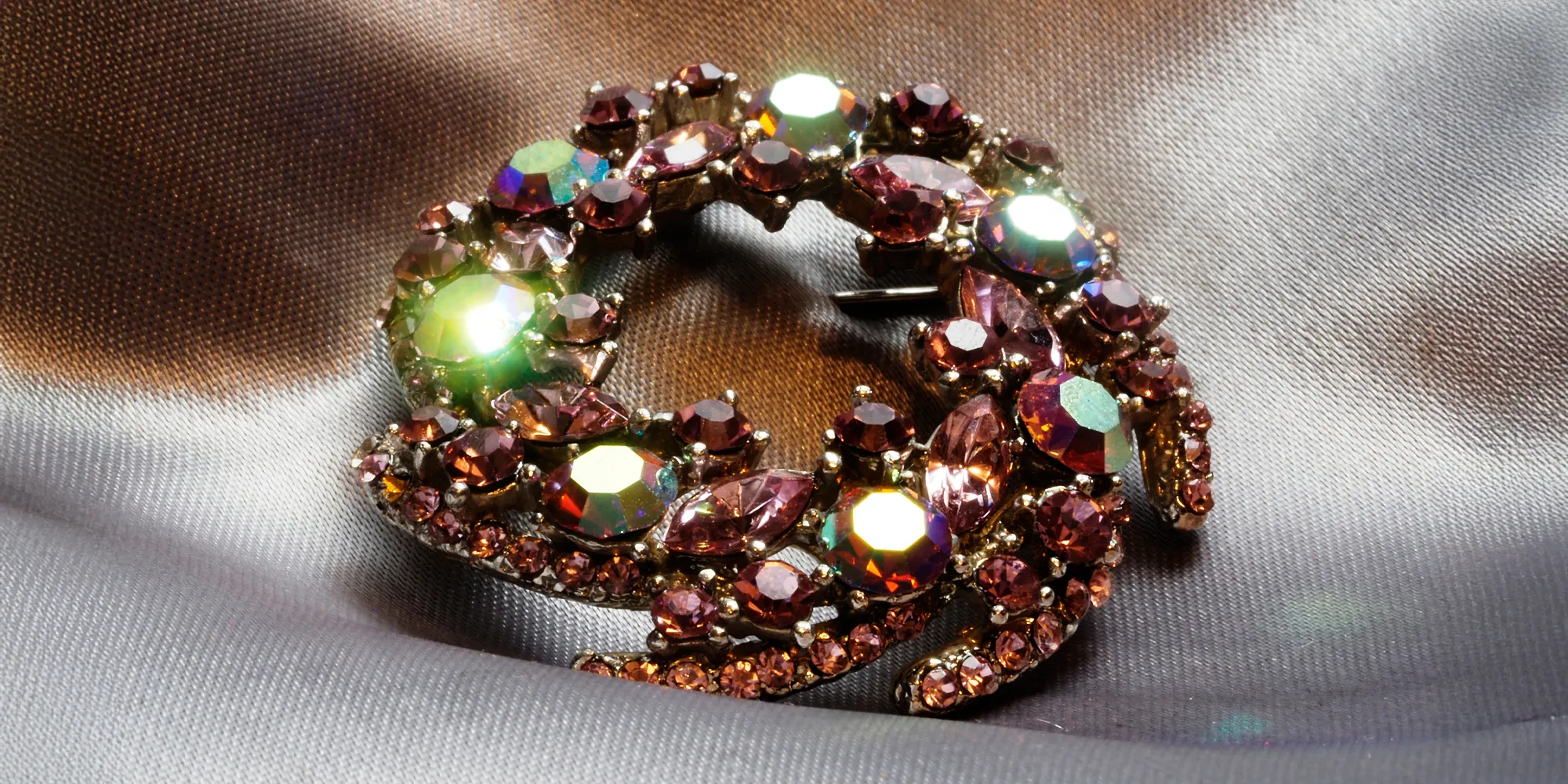 Sparkling vintage brooch with pink and iridescent stones on a silky background.