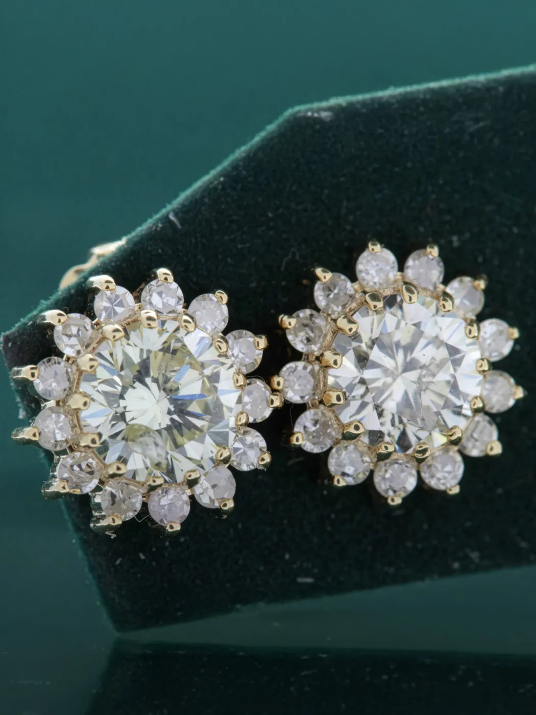 Sparkling diamond earrings with a floral design, set in gold, displayed on a green velvet background.
